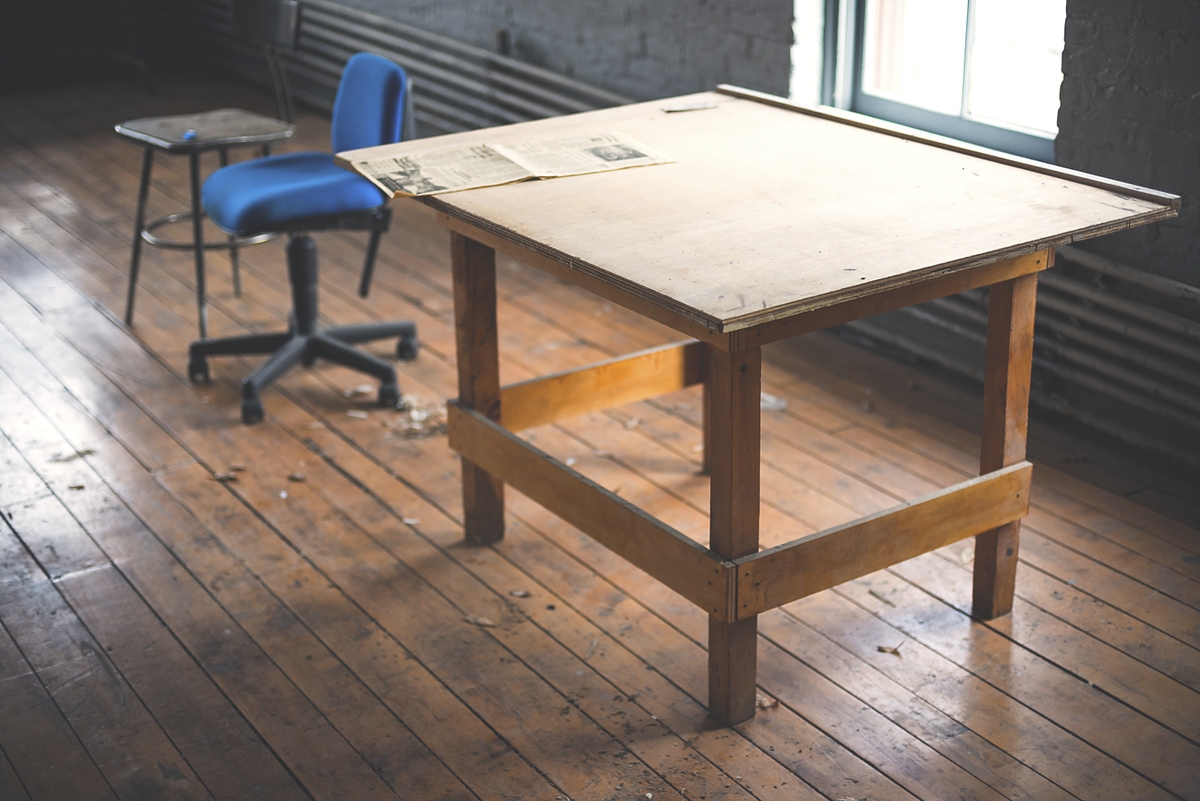 An old table near a blue office chair in a messy room. Original public domain image from Wikimedia Commons